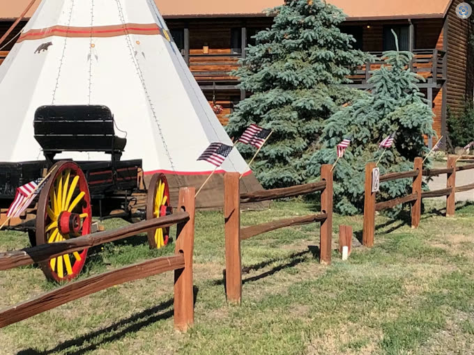 A full-size tipi standing on the lawn beside an antique wagon